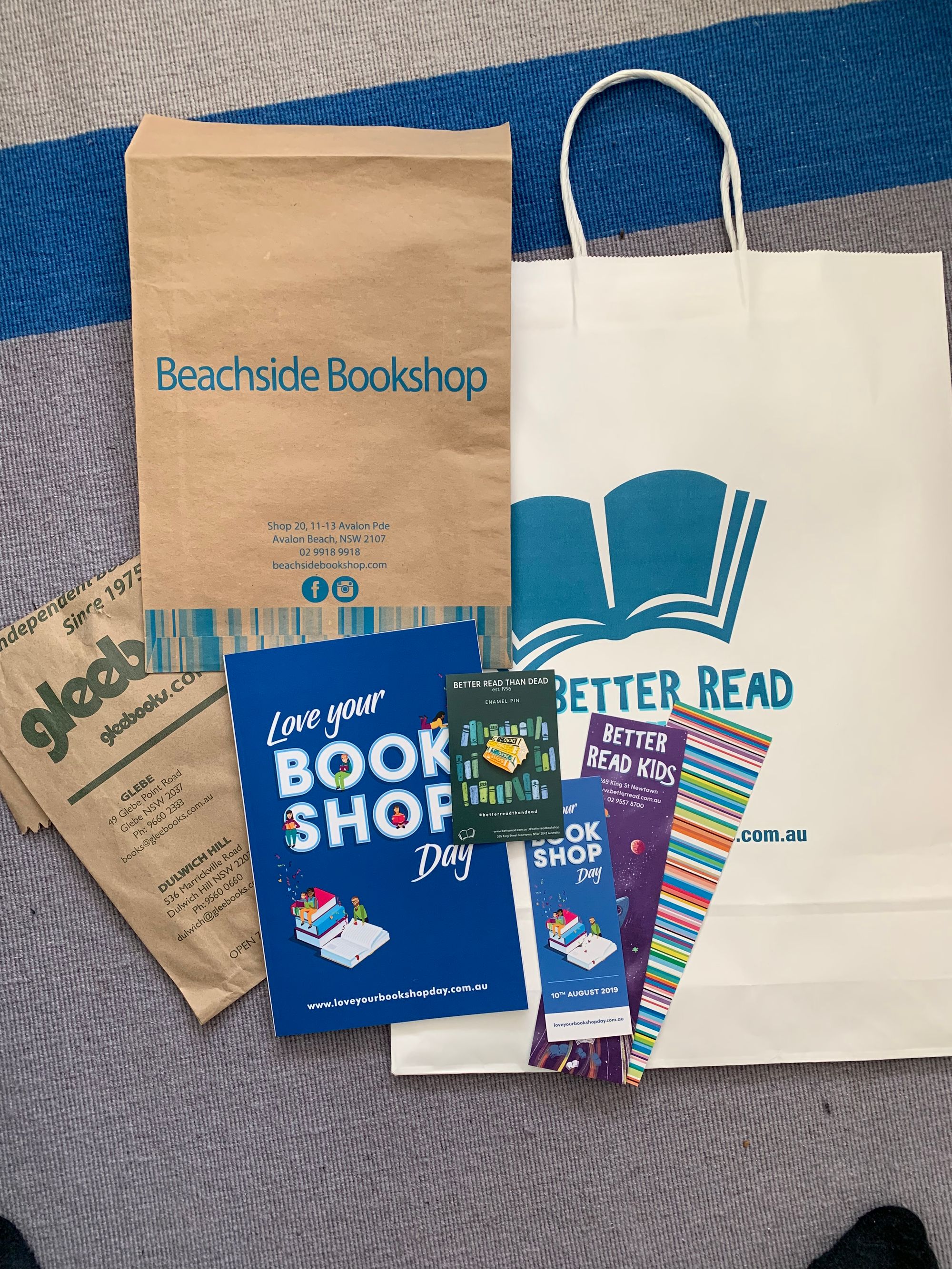 Photo of three bookstore paper bags, a love your bookshop day notebook, three bookshop branded bookmarks and a Better Read Than Dead enamel pin